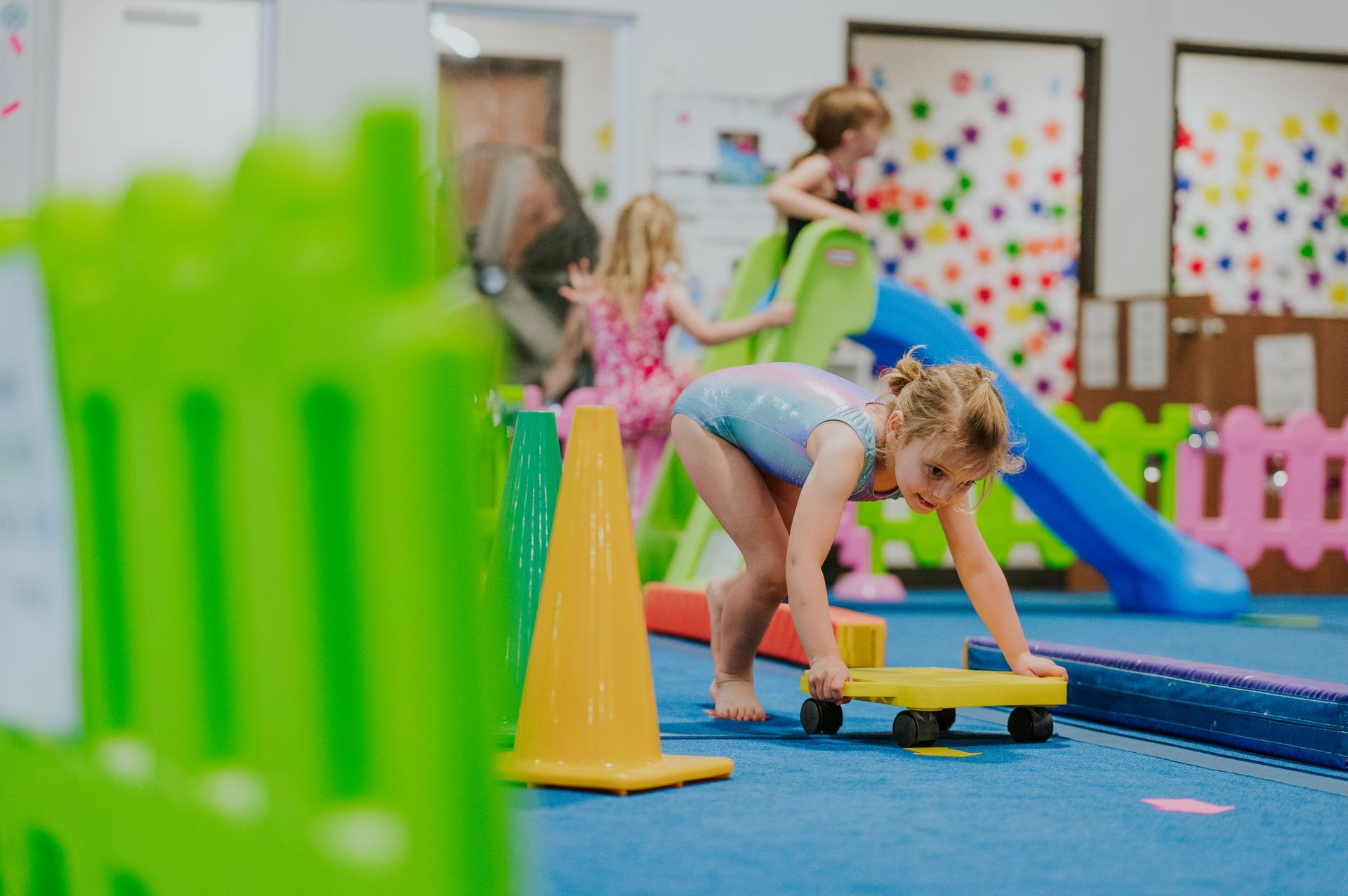 Children playing on colorful indoor soft-play equipment with cones, a tunnel, and a slide.