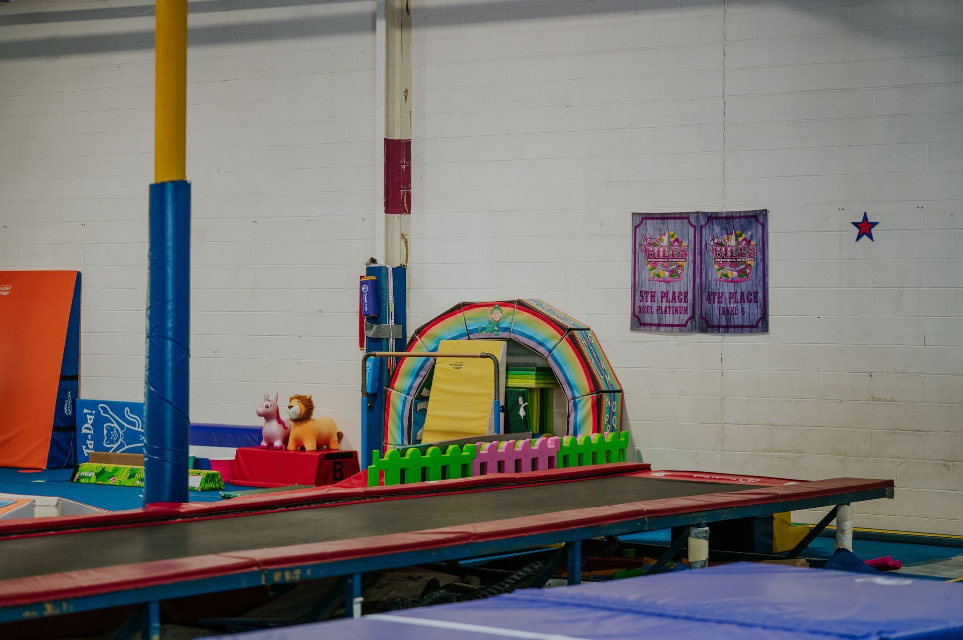 Colorful indoor play gym with a rainbow arch, foam blocks, and mats on a padded floor