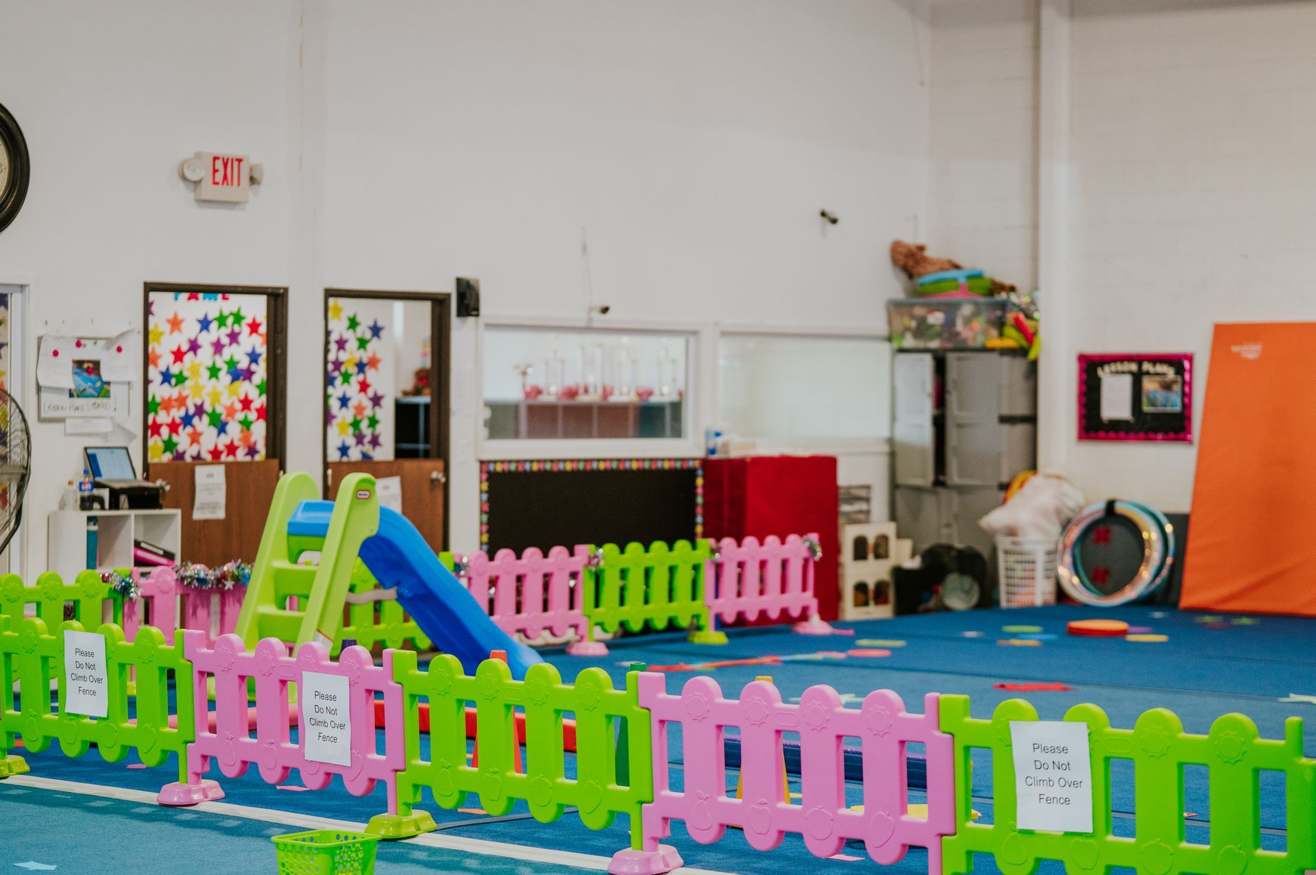 Colorful playroom with toy fence, slides, playhouses, and climbing equipment on a blue floor