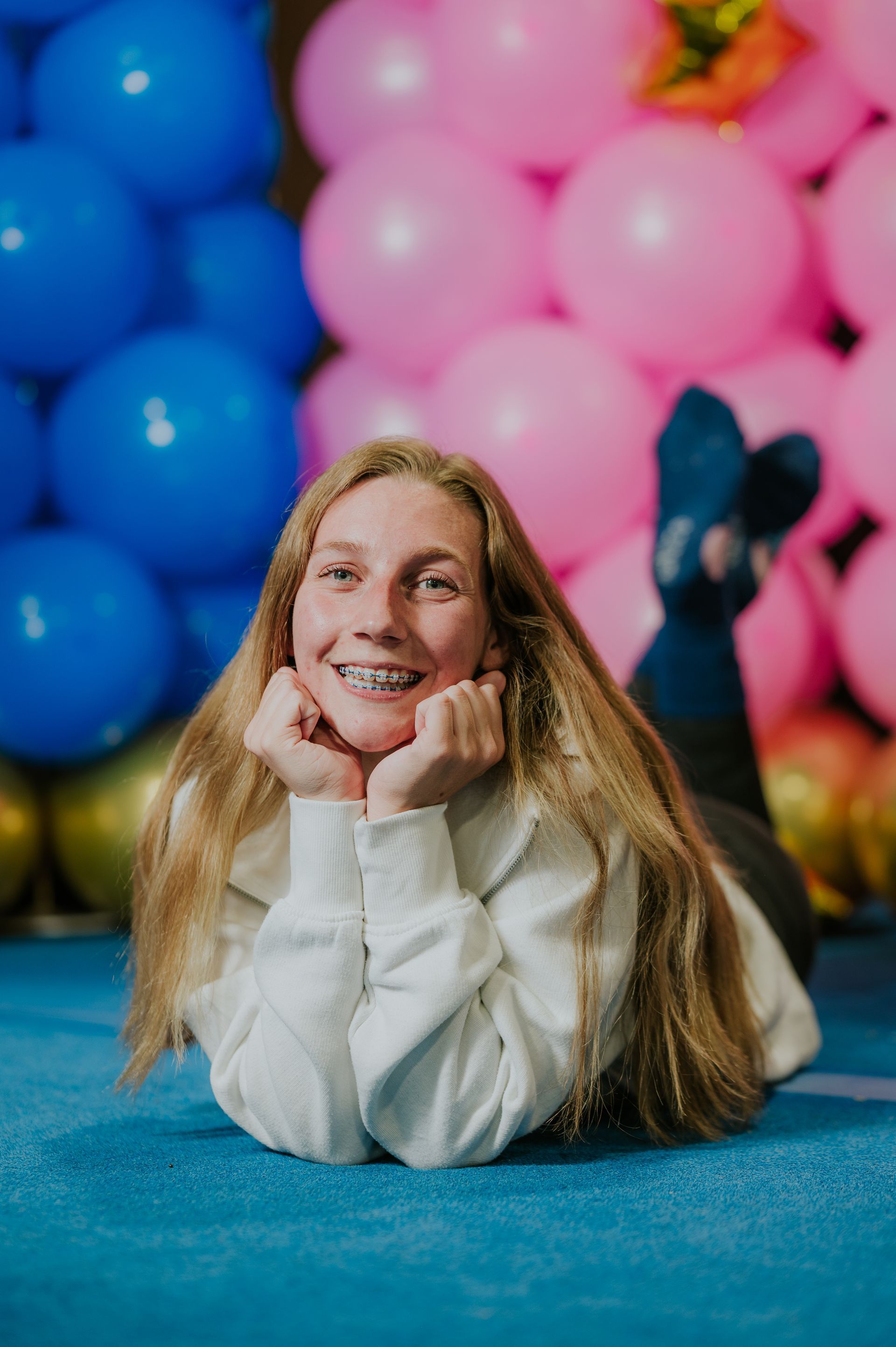 Smiling person lying on blue carpet in front of pink and blue balloons
