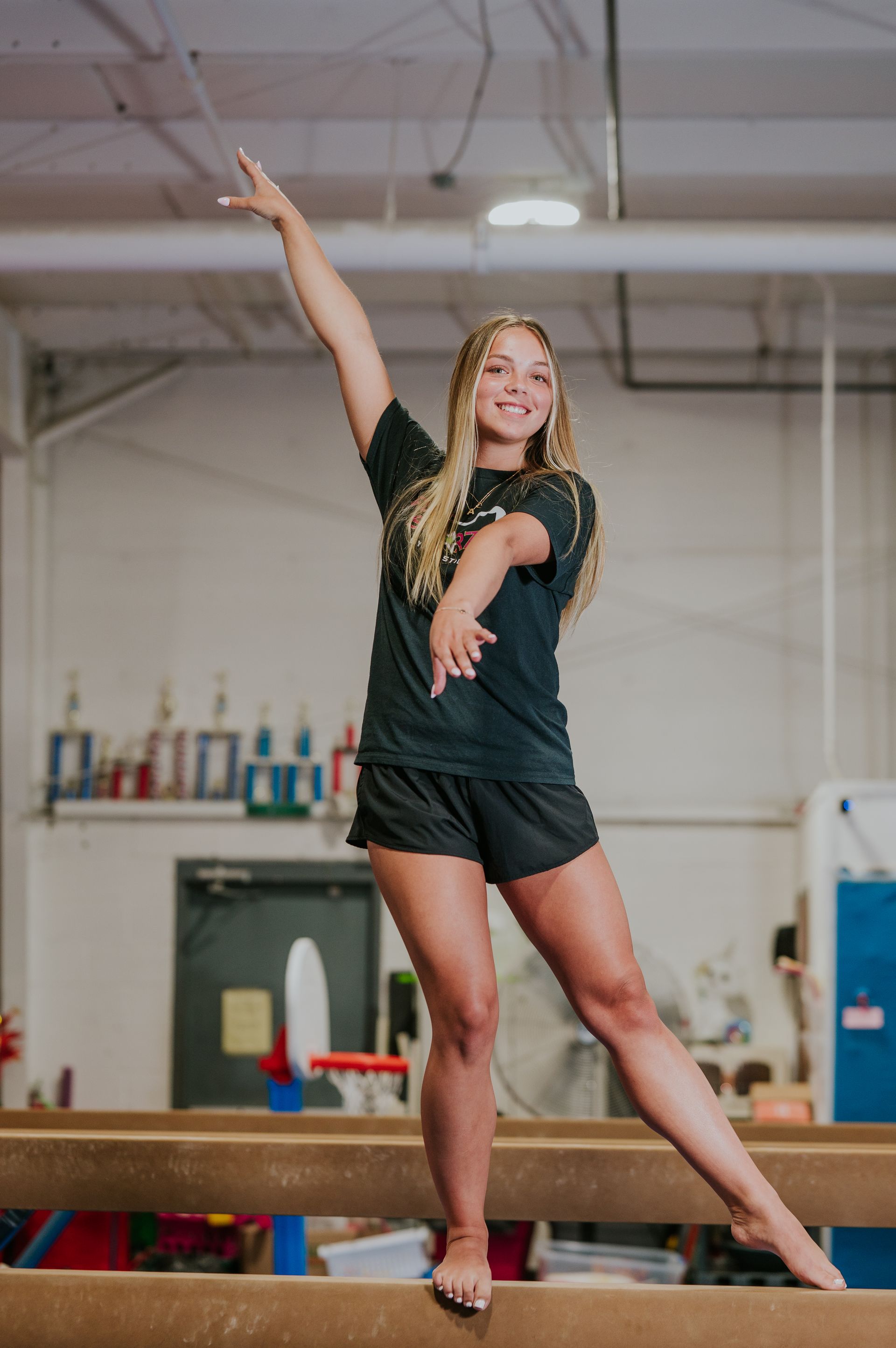 Gymnast balancing on a beam, one arm raised, in a gymnasium.