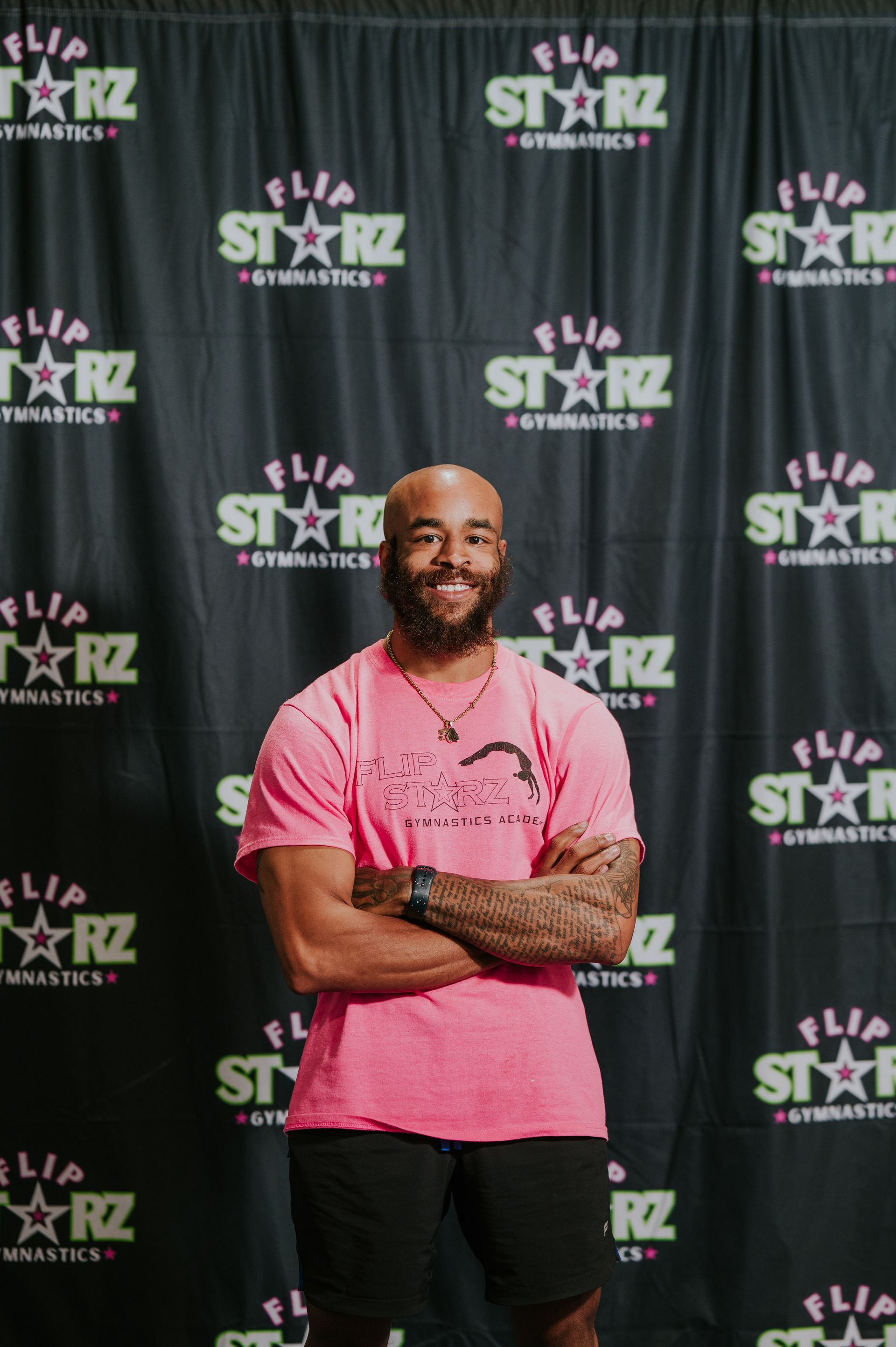 Man standing with arms crossed in a pink shirt before a black STARZ backdrop