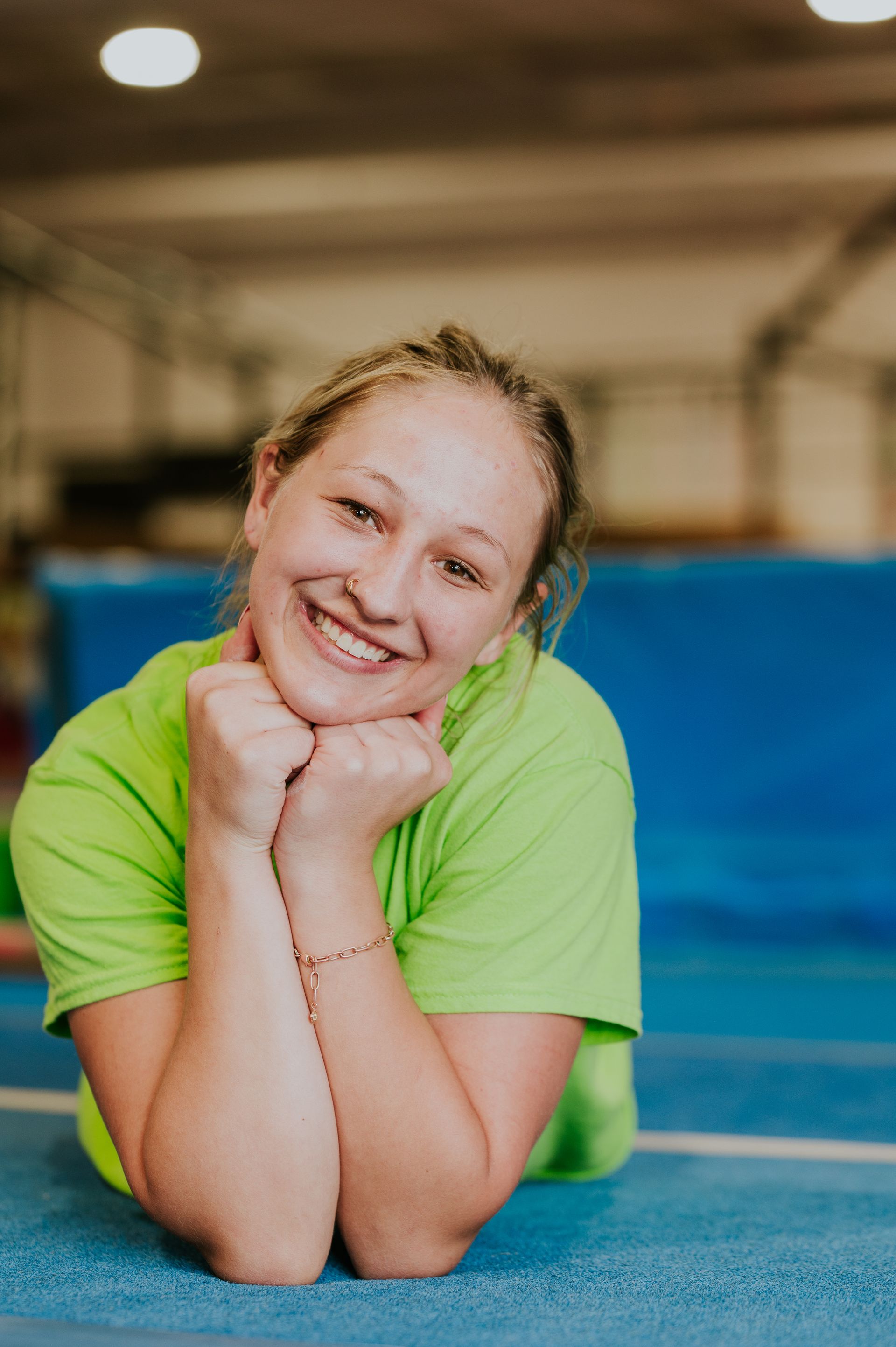 Smiling person in a green shirt leaning on elbows on a blue gym mat