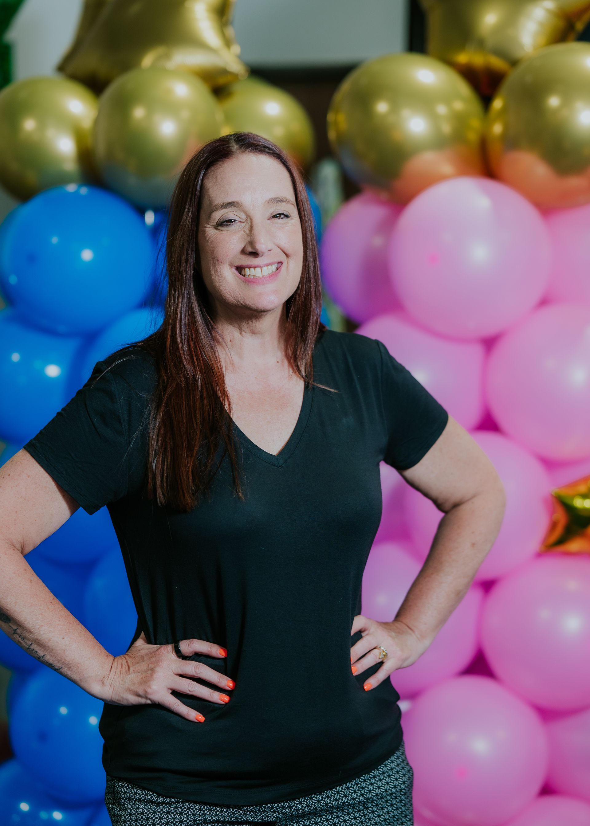Woman smiling with hands on hips in front of colorful balloon backdrop