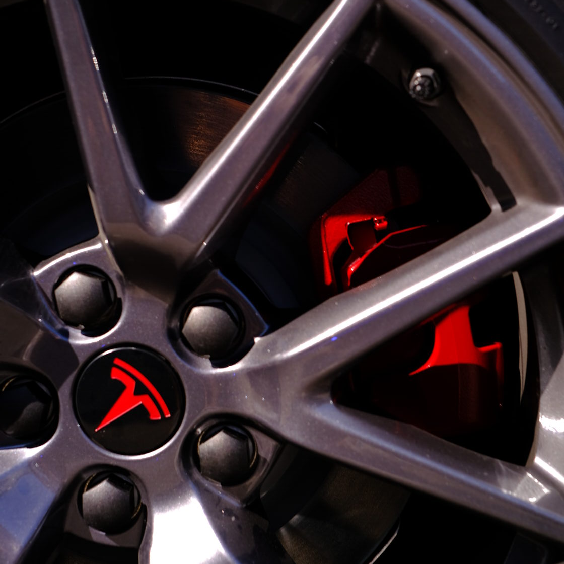 A close up of a tesla wheel with a red logo on it