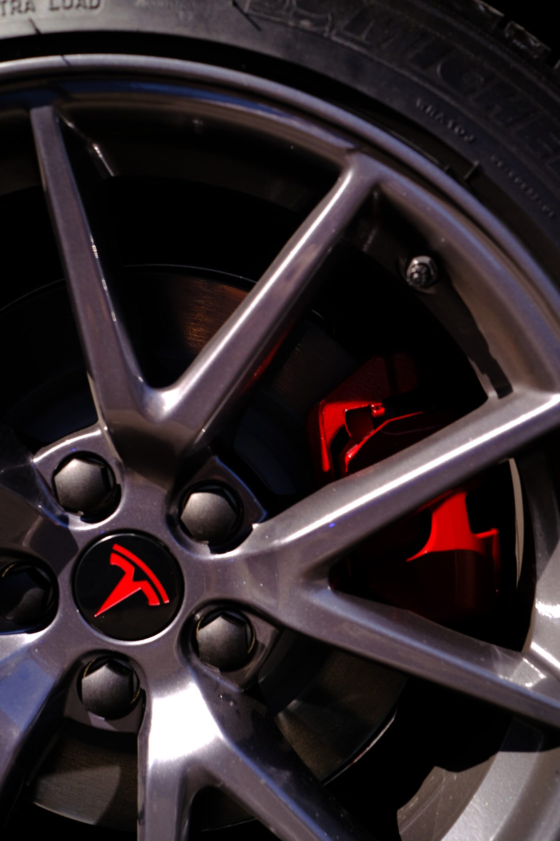A close up of a tesla wheel with a red Tesla logo at XWRAPS, a professional Vinyl Car Wrap service provider in LA.