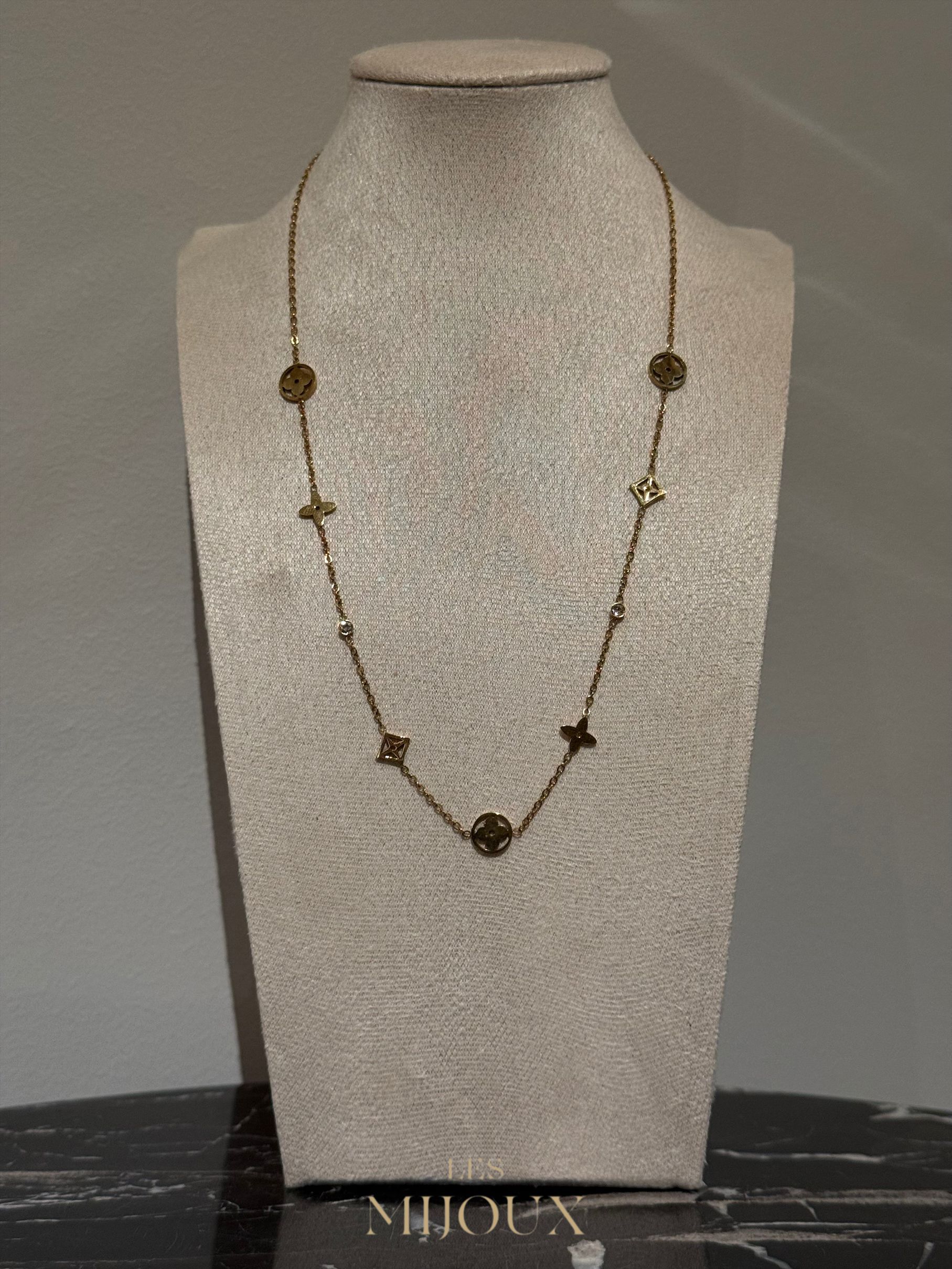 Gouden halsketting met ronde en kruisvormige bedeltjes, tentoongesteld op een beige paspop tegen een neutrale achtergrond.