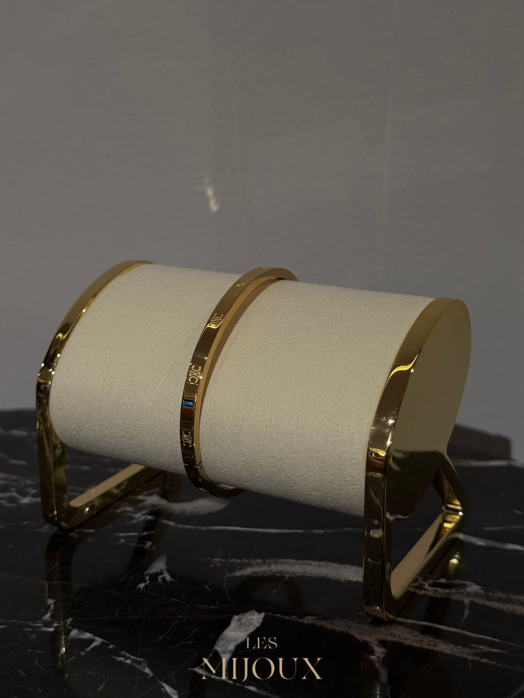 Gouden armbanden op een crèmekleurige displaystandaard, geplaatst op een marmeren ondergrond.