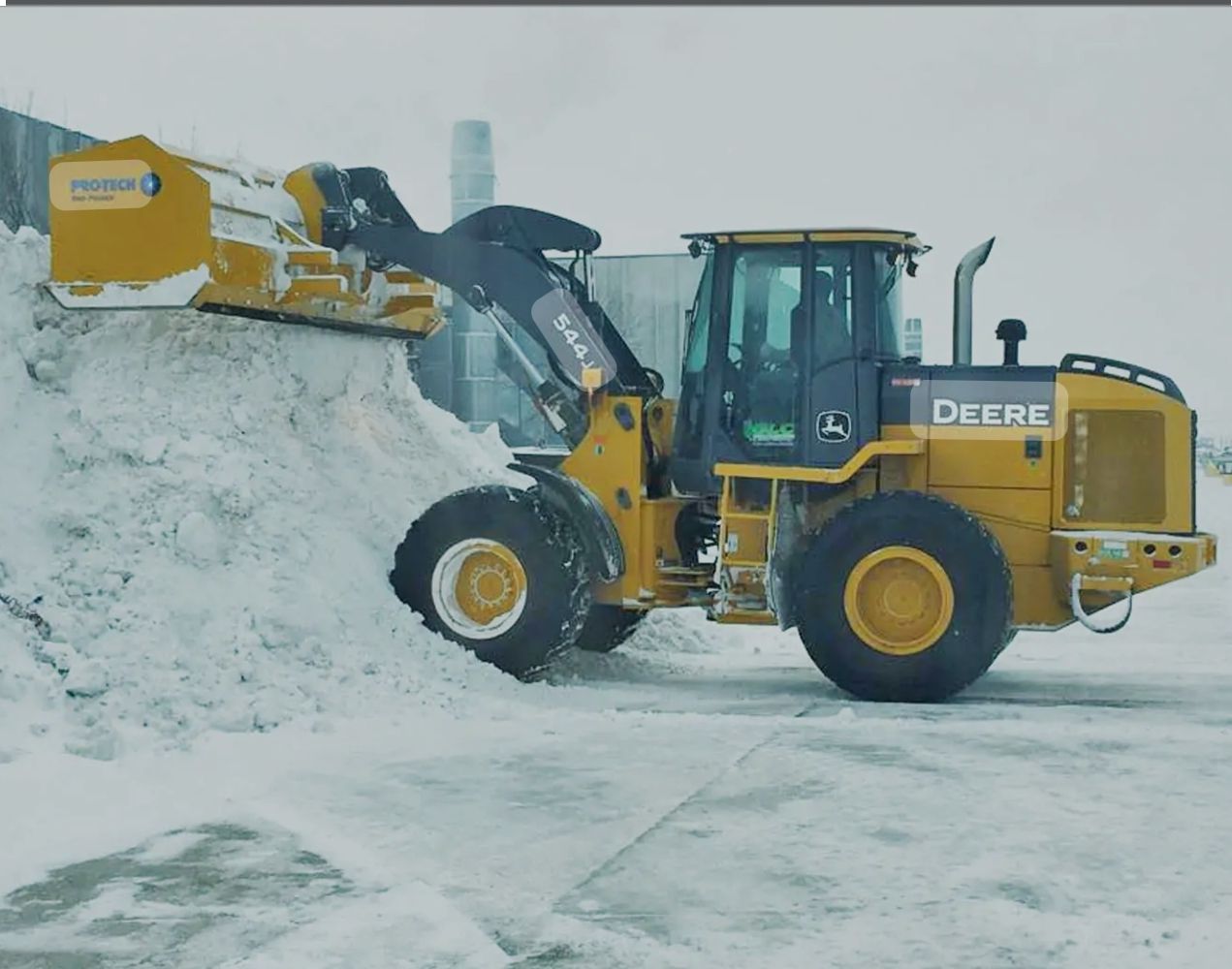 A deere wheel loader is loading snow into a pile