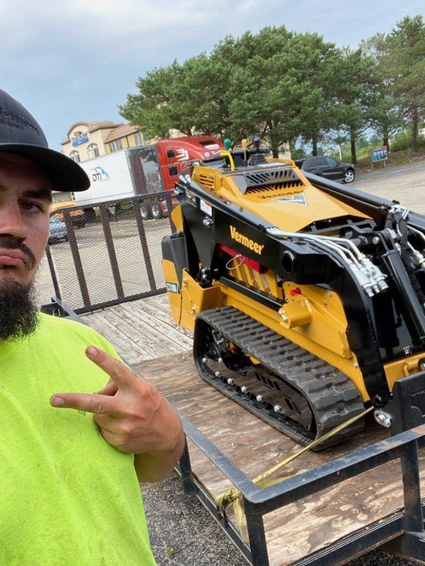 A man with a beard is standing next to a tractor on a trailer.