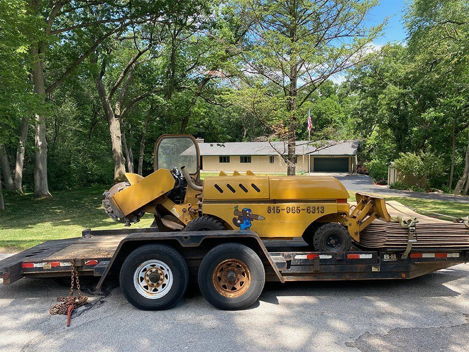 A yellow tractor is on a trailer parked in front of a house.
