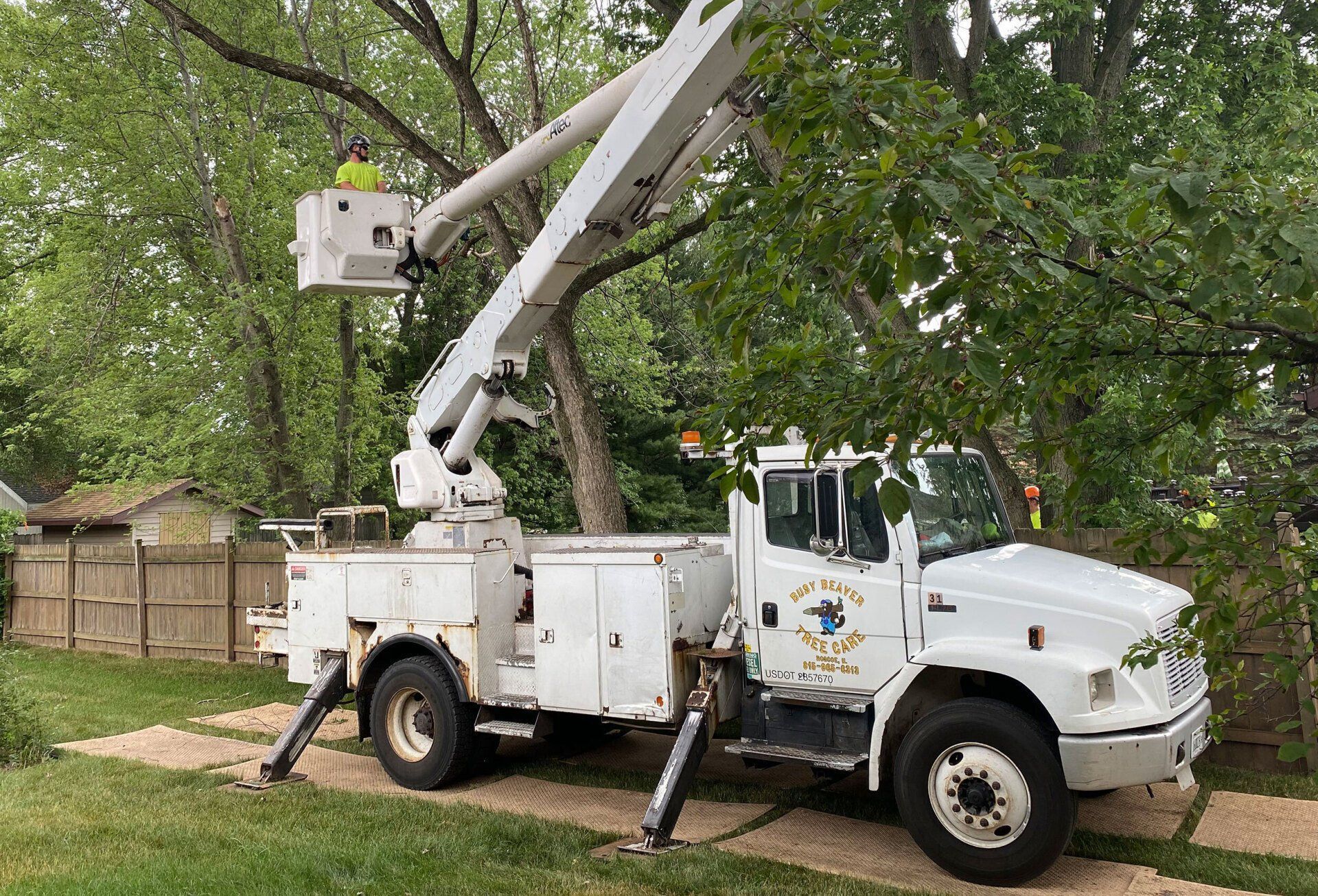 A white truck with a crane attached to it is parked in front of a tree.