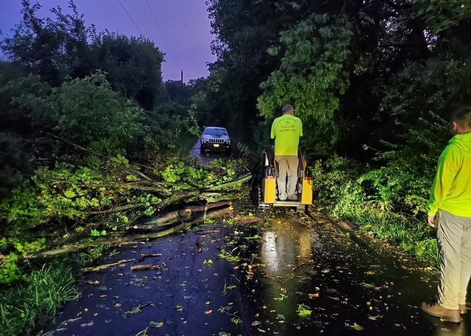 A man in a green shirt is pushing a tractor down a flooded road.