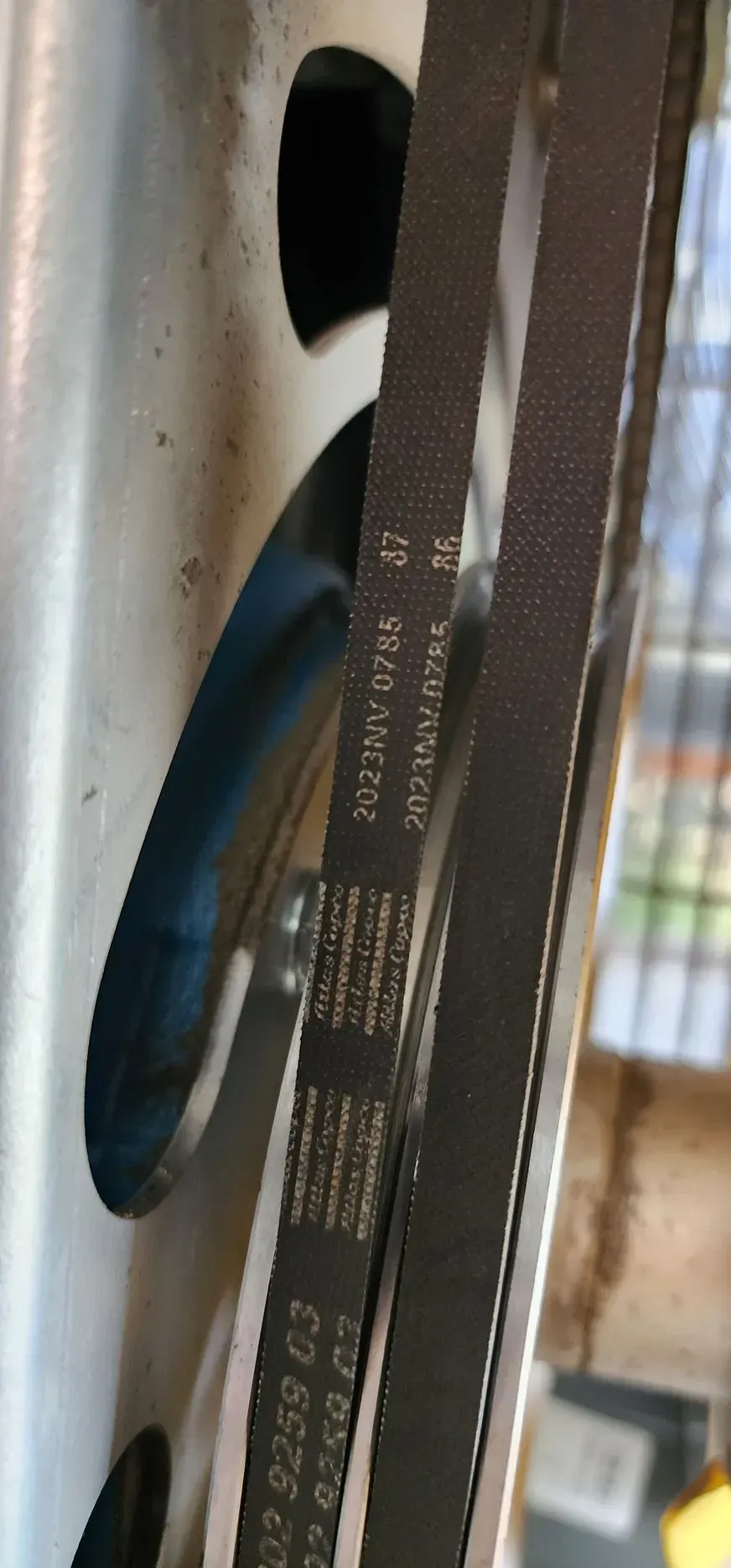 Two dark belts on a pulley. The belts have white text. Metal casing surrounds the pulley.