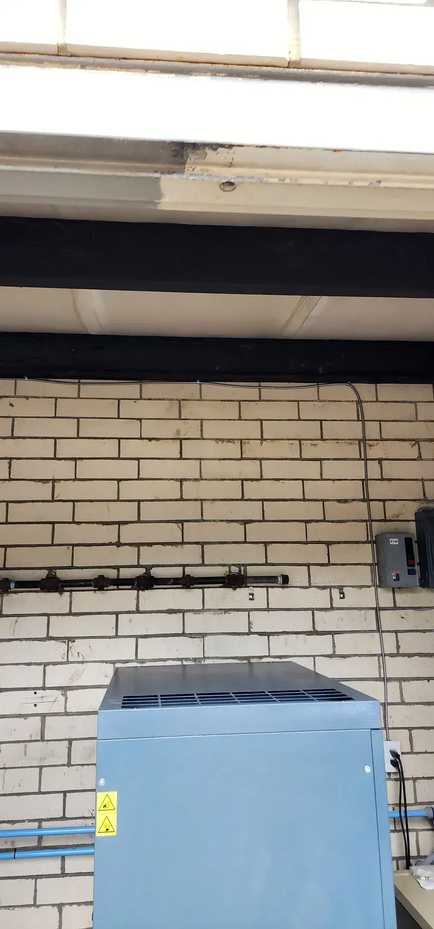 Blue appliance against a white brick wall, under a white ceiling and black beams.