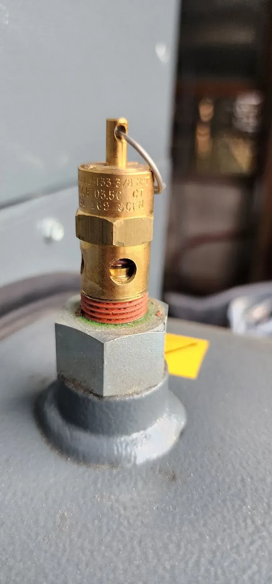 Close-up of a brass pressure relief valve on a gray tank, with a safety ring attached.