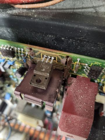 Circuit board with a transistor, a red connector, and dust accumulation.