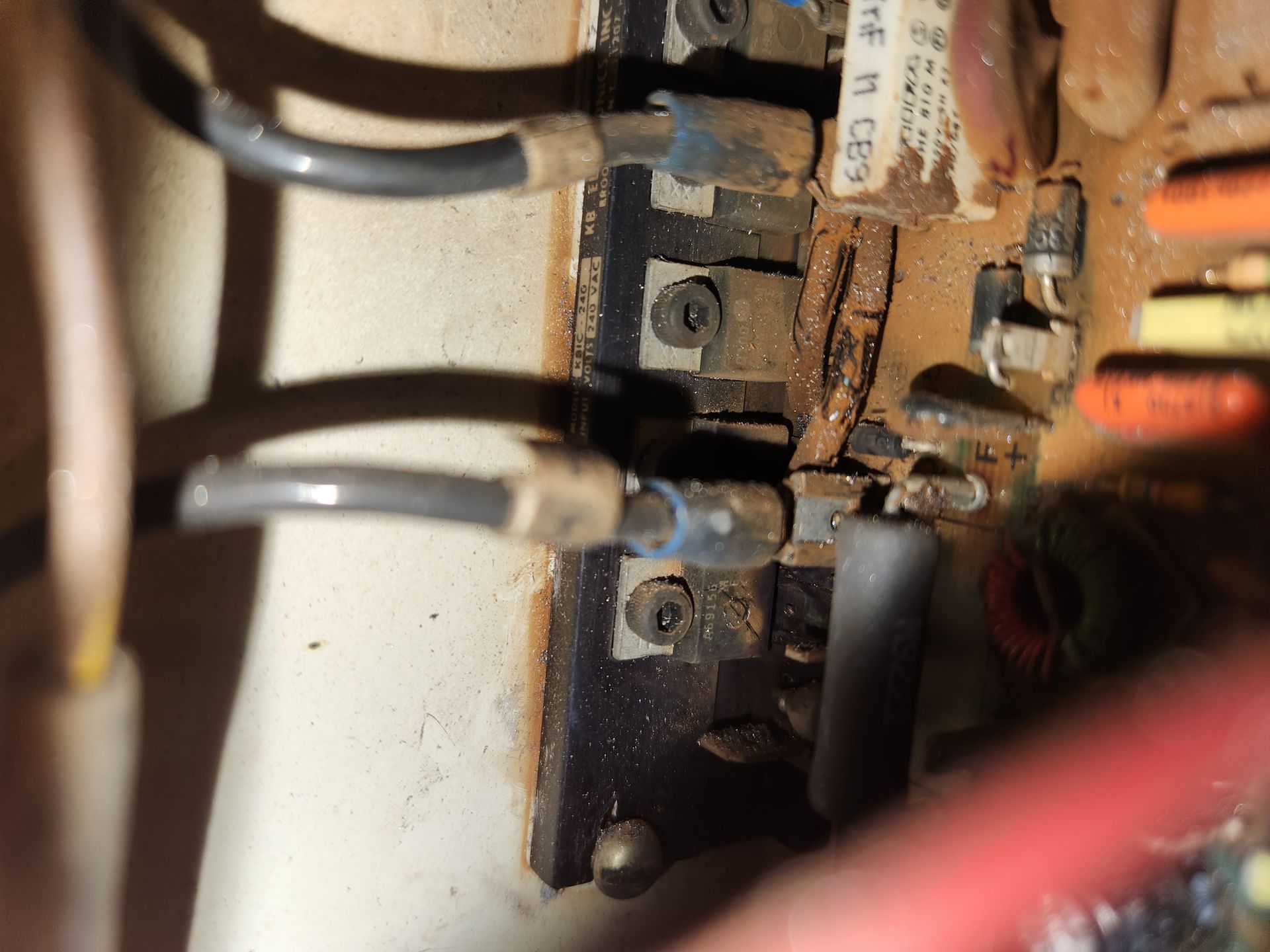 Close-up of an electrical circuit board with damaged components, visible wires, and screws covered in dust.