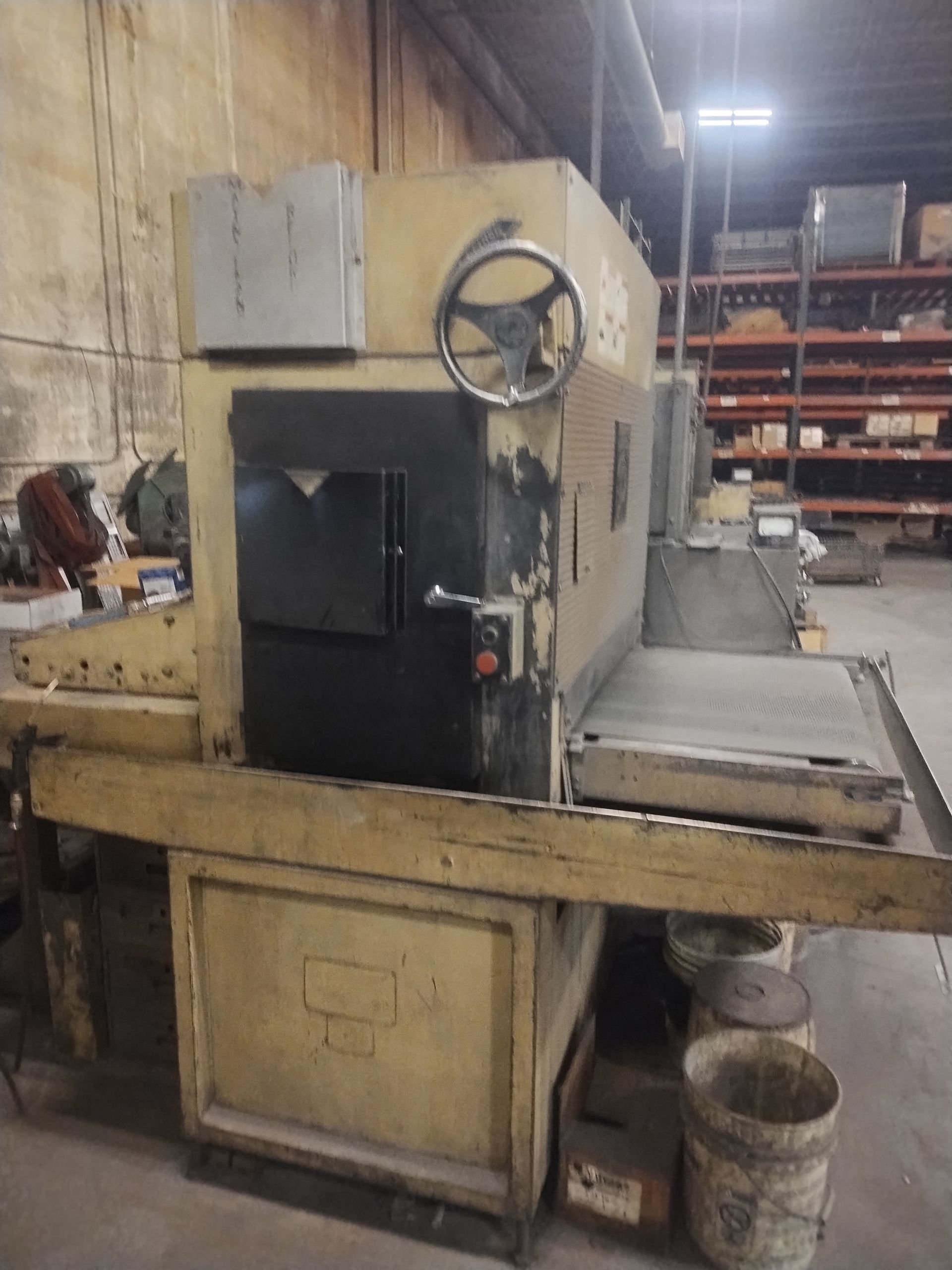 Yellow industrial machine with a large, dark door and a hand crank in a warehouse.