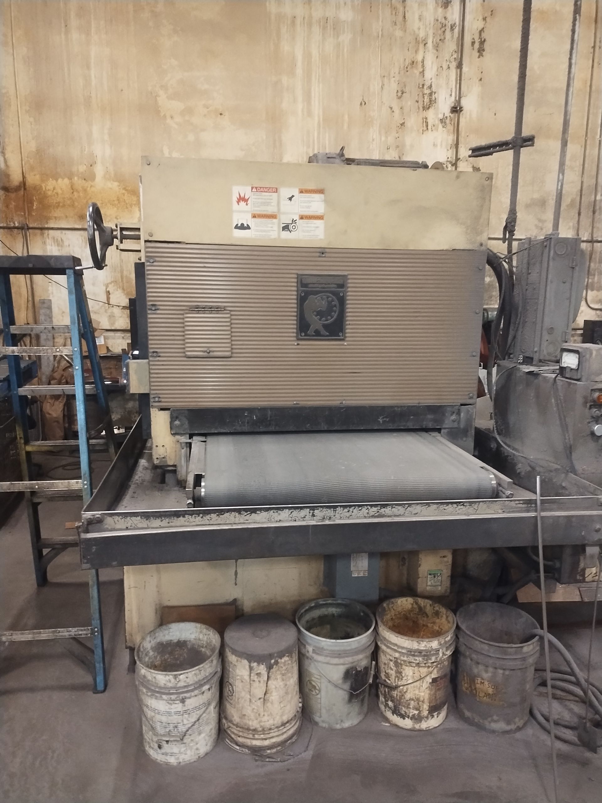 Large industrial sander machine in a workshop, with buckets underneath.