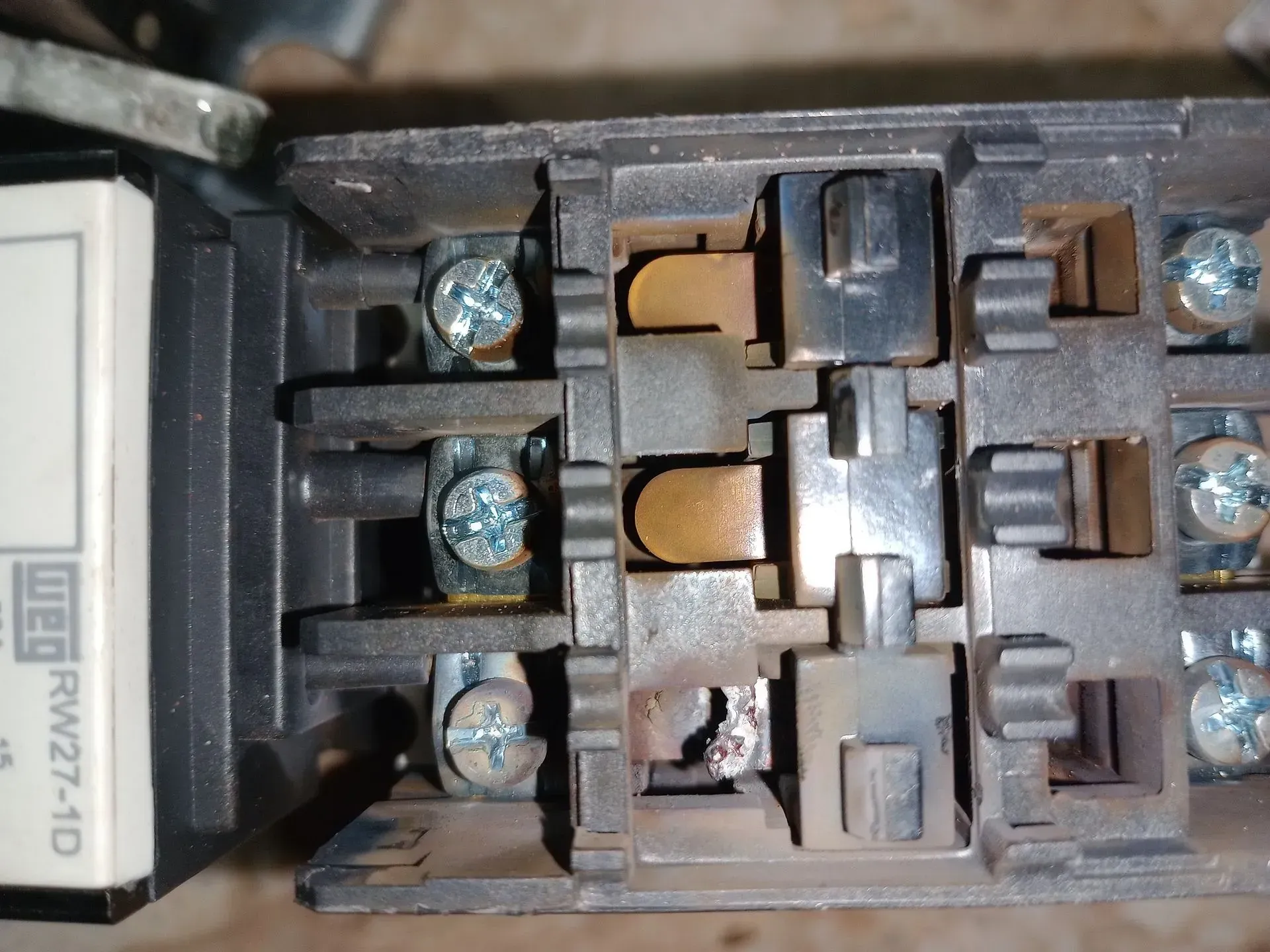 Close-up of a damaged electrical contactor. Burnt components and screws are visible.