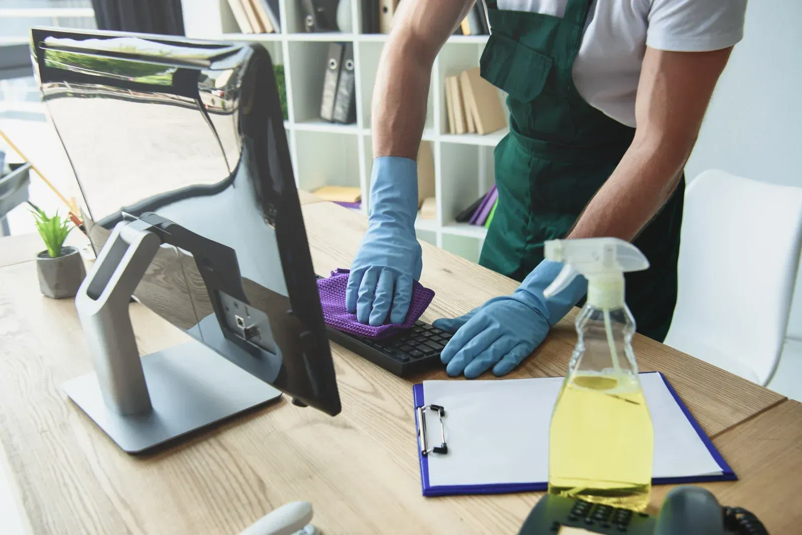 Person cleaning a computer keyboard with a purple cloth and spray bottle.