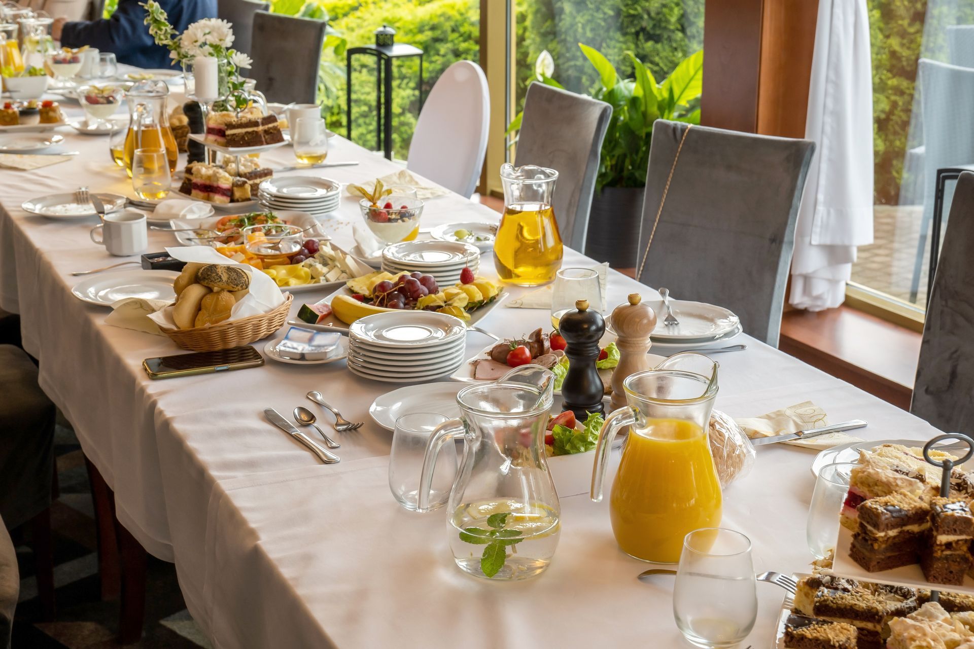 Long dining table set with food and drinks, near a window.