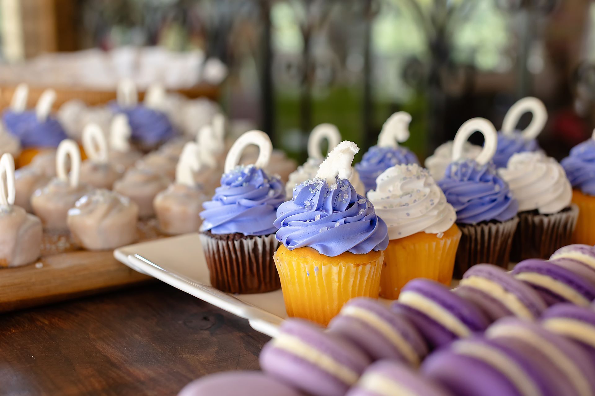 Dessert table with purple frosted cupcakes, cake pops, and macarons.