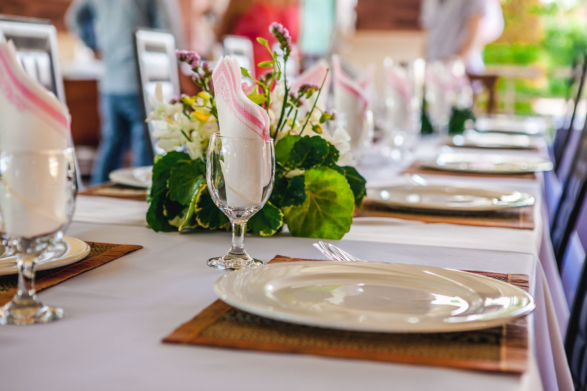 Table setting with white tablecloth, plates, glasses, and floral centerpiece.