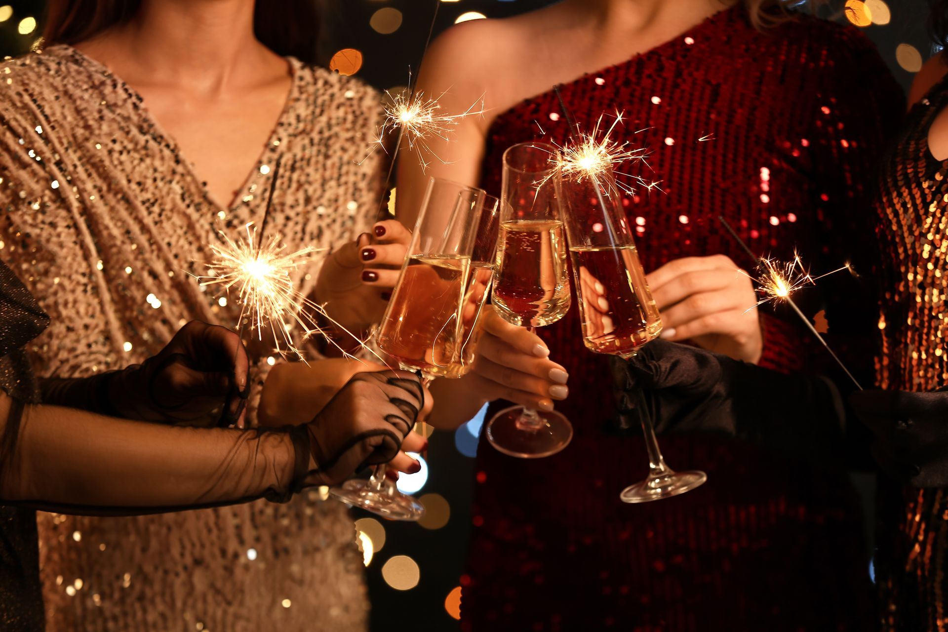 Women toasting champagne flutes, wearing sequined dresses, holding sparklers at a festive gathering.