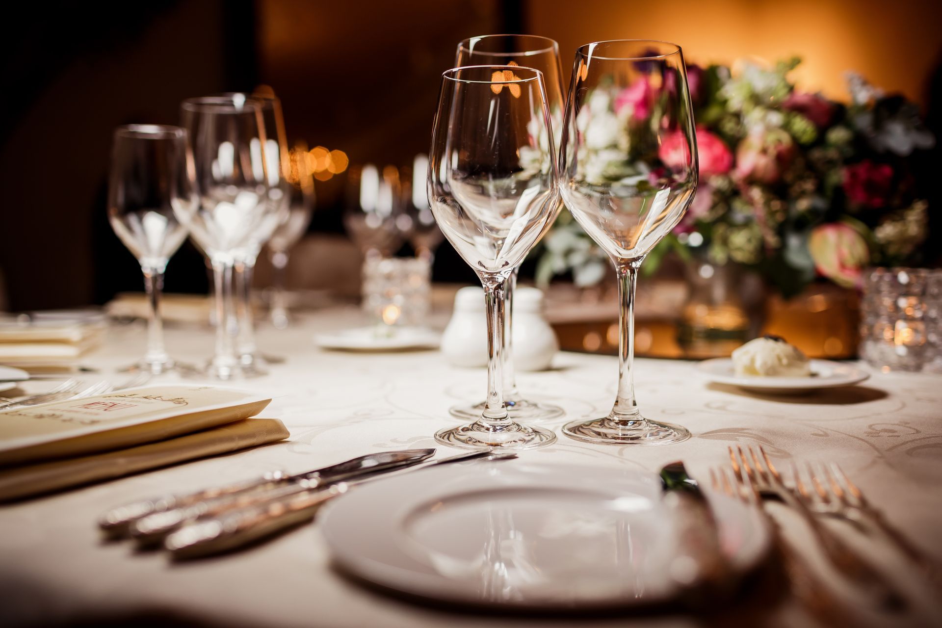 Elegant table setting with wine glasses, plates, silverware, and floral arrangement.
