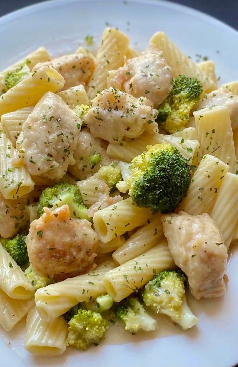 Pasta dish: rigatoni, chicken pieces, broccoli florets, creamy sauce, sprinkled with herbs.