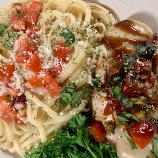 Spaghetti with tomato, parsley, and parmesan cheese, alongside chicken with sauce and herbs.