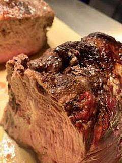Close-up of a cooked, seared roast beef, revealing juicy pink interior and dark, crispy exterior.
