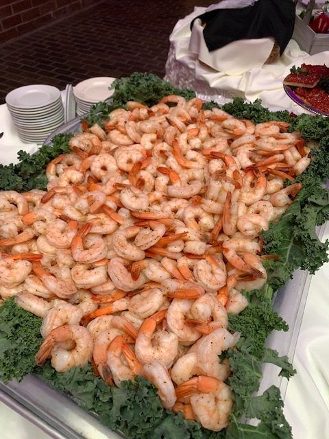 Shrimp platter on kale, ready to serve, set at an event with plates nearby.