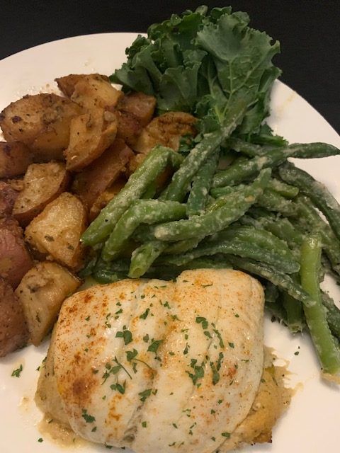 Plate of food with roasted potatoes, green beans, kale, and a piece of white fish.