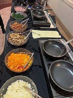 Buffet with various ingredients in bowls and frying pans on a table.