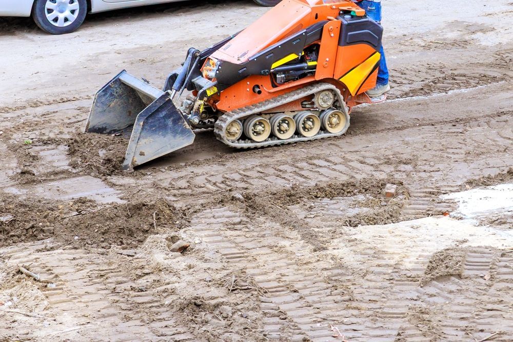 Orange skid-steer loader pushing mud on a muddy construction site