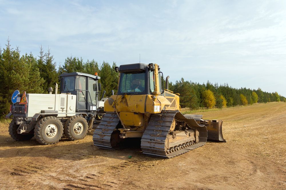 Bulldozer and dump truck parked on a dirt road in a forest clearing