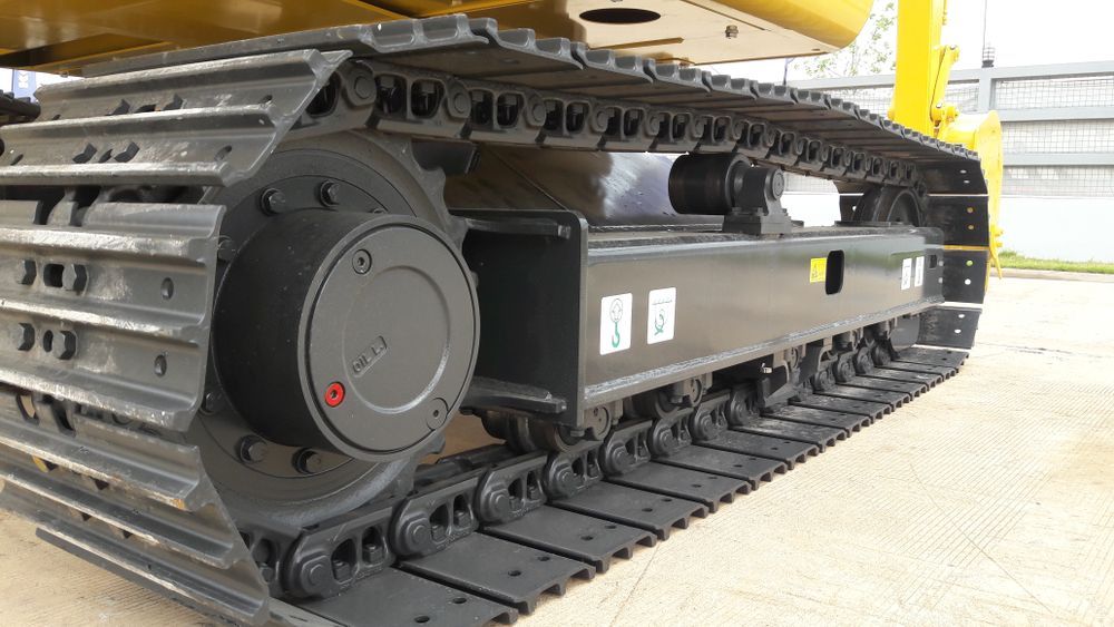 Close-up of a yellow excavator’s tracked undercarriage and hydraulic components on a concrete surface