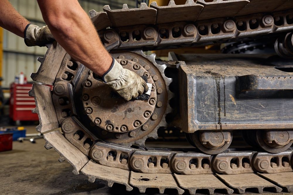Gloved hand inspecting a tank’s track and wheel assembly in a workshop