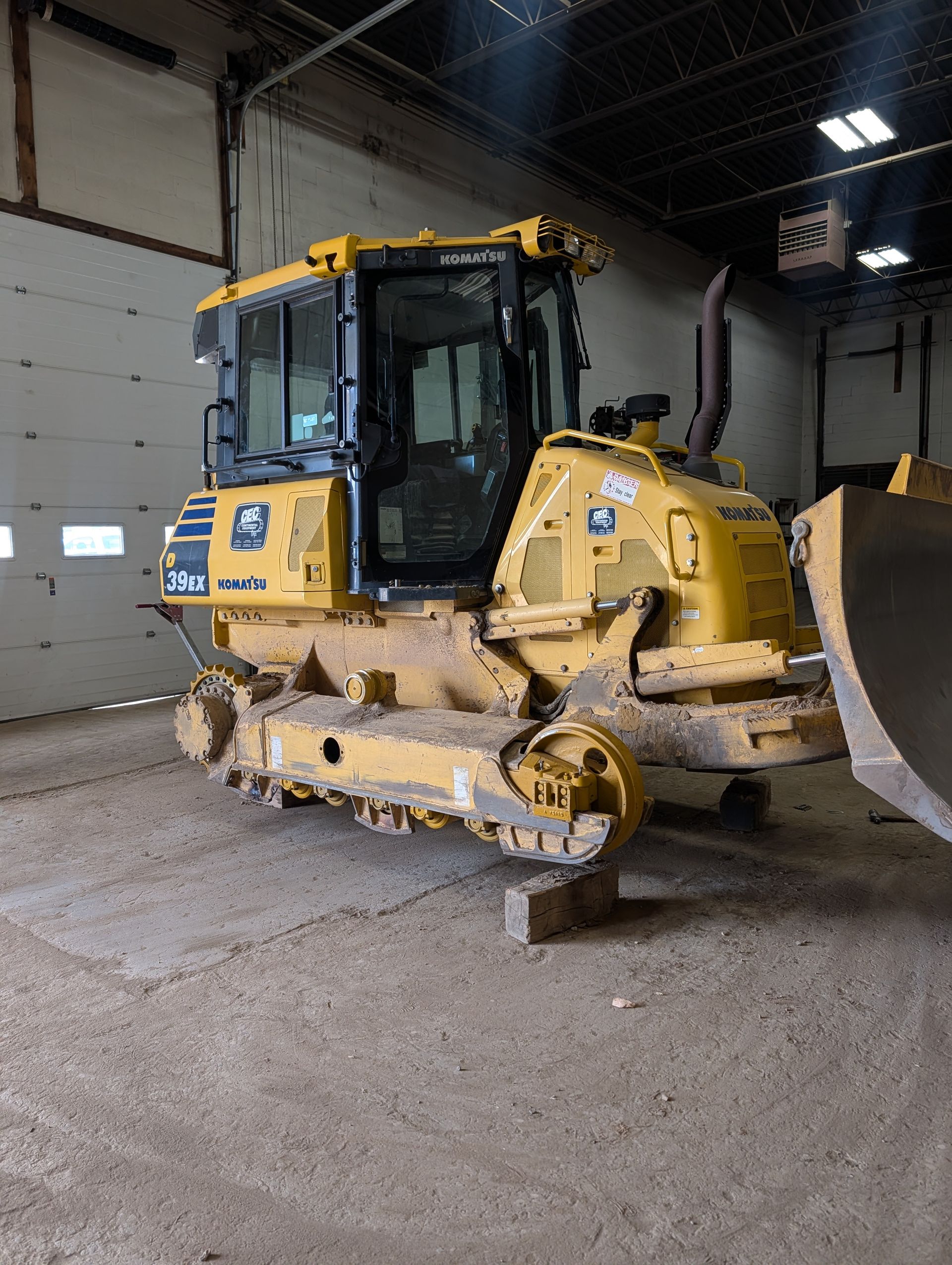 Yellow Caterpillar bulldozer parked indoors on a gravel floor in a warehouse-like garage.