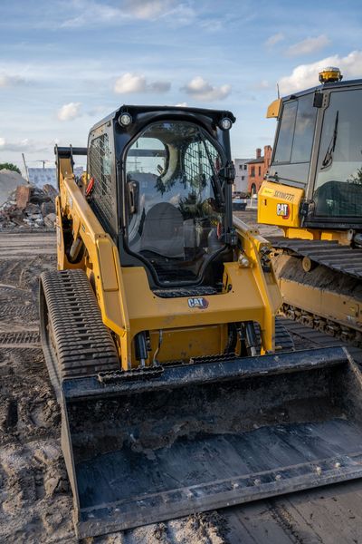 Yellow skid steer loader with muddy bucket at a construction site under a cloudy sky