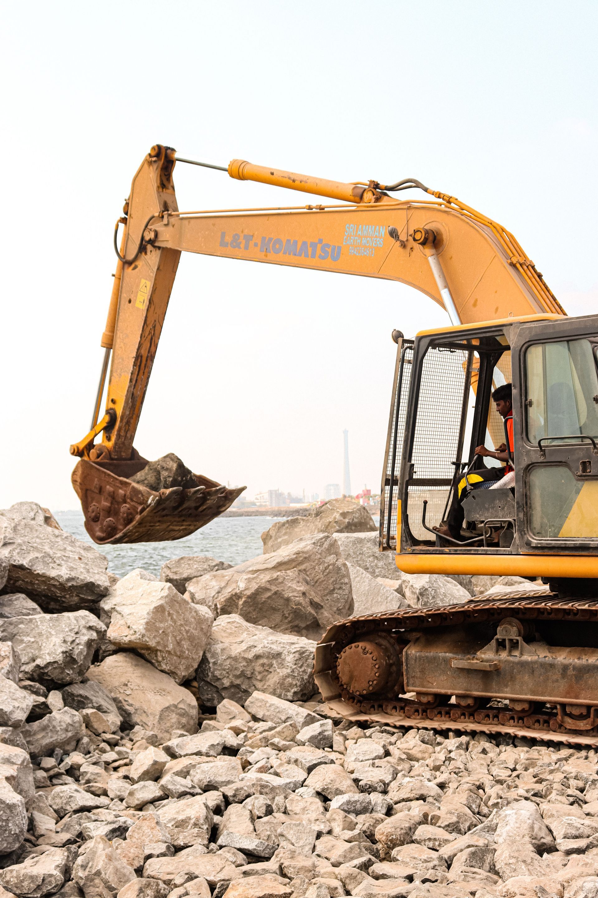 Yellow excavator digging through a pile of large rocks at a construction site