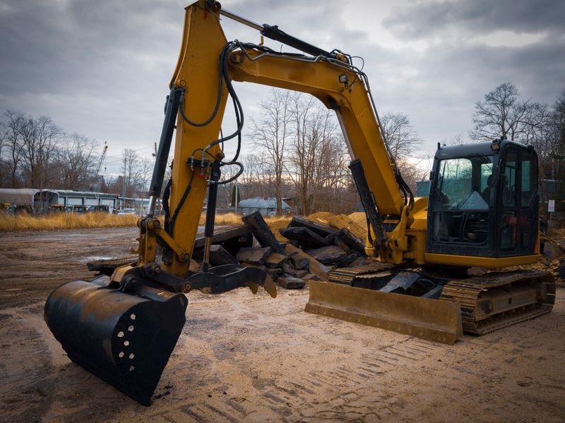 Yellow excavator on a muddy construction site with a bucket and scattered debris.