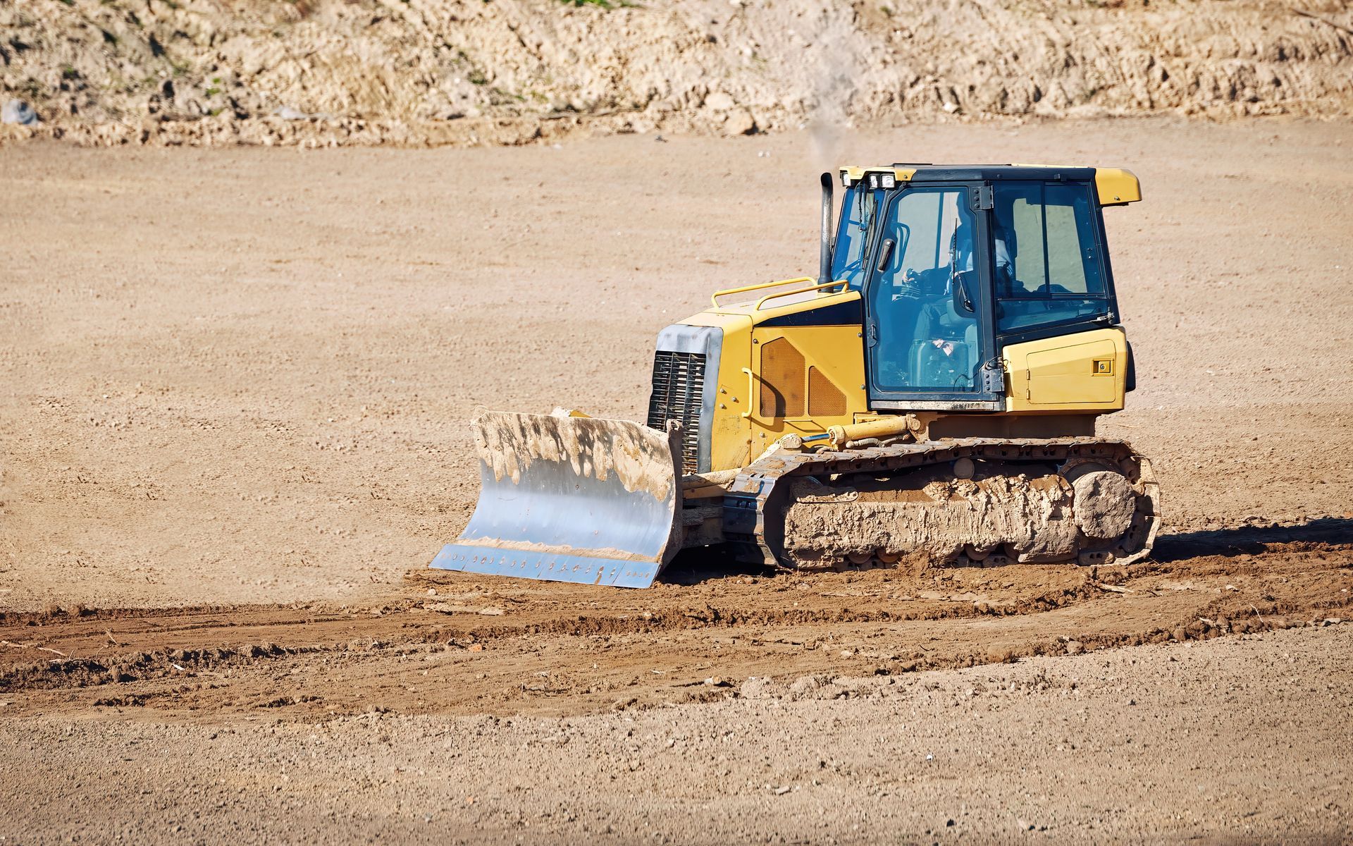 Yellow bulldozer pushing dirt on a construction site with a rocky embankment in the background