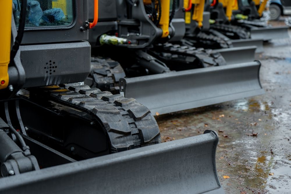 Close-up of tracked construction vehicles with front blades lined up on a wet street