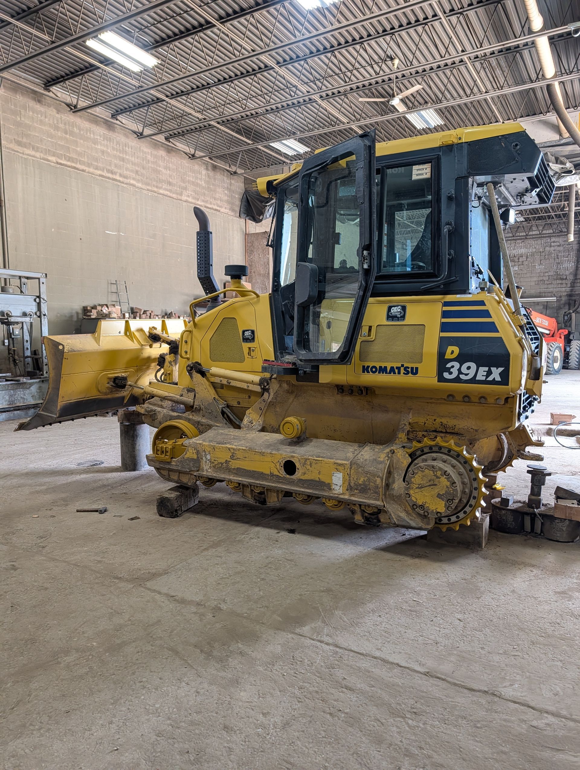 Yellow tracked bulldozer inside an industrial warehouse with a high metal ceiling.