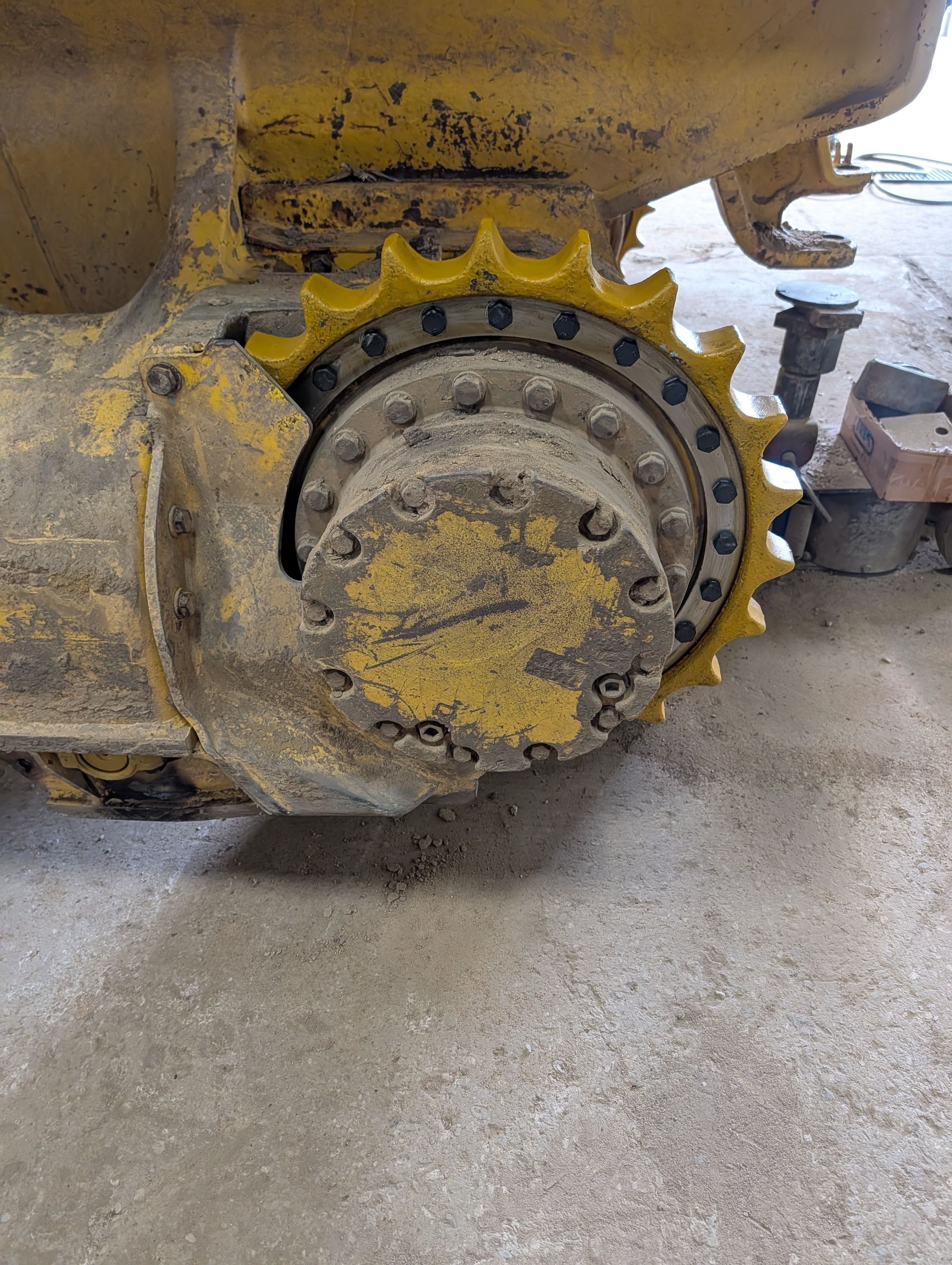 Close-up of a muddy yellow excavator track sprocket and undercarriage on concrete.