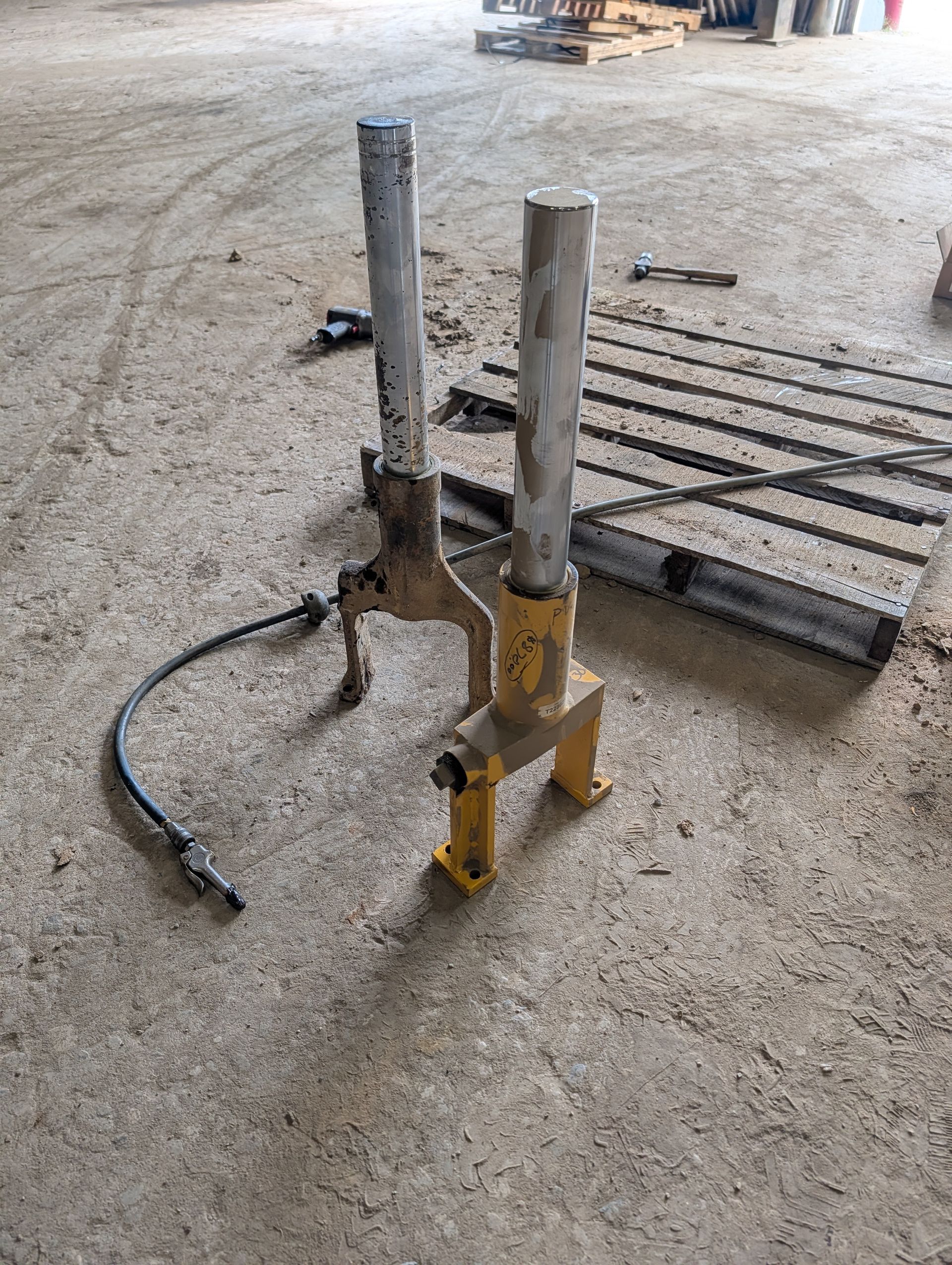 Two upright metal pipes on a concrete floor beside a grated drain and cable in an industrial setting